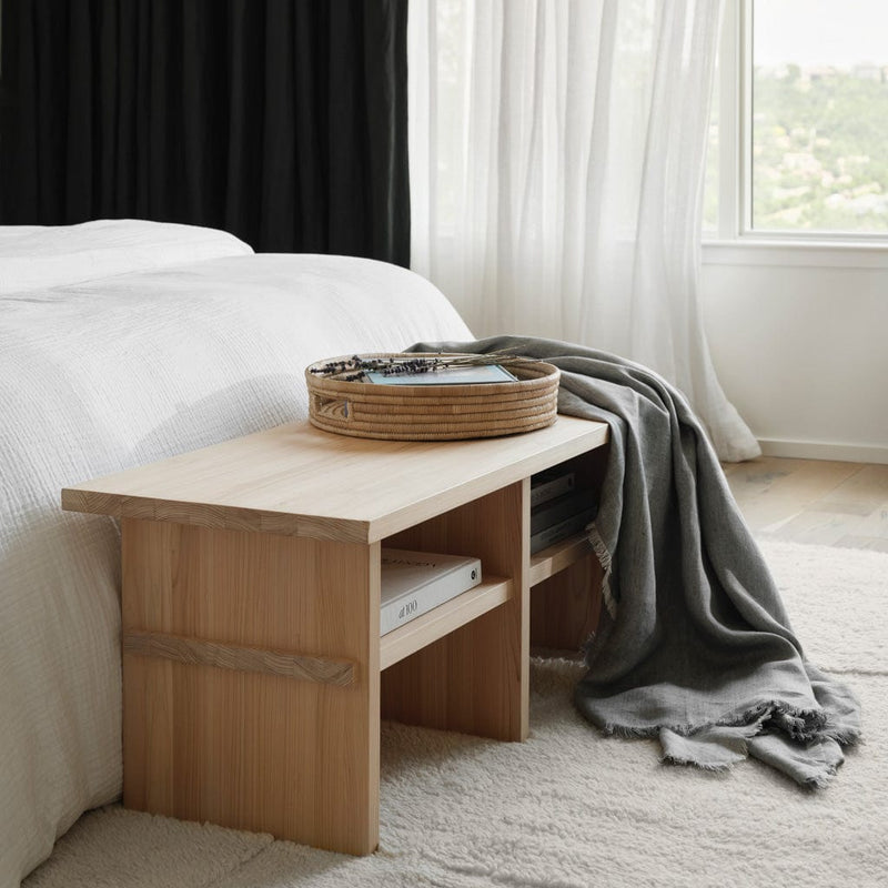 Close up of hinoki wood bench at the foot of a bed styled with books and a tray, natural