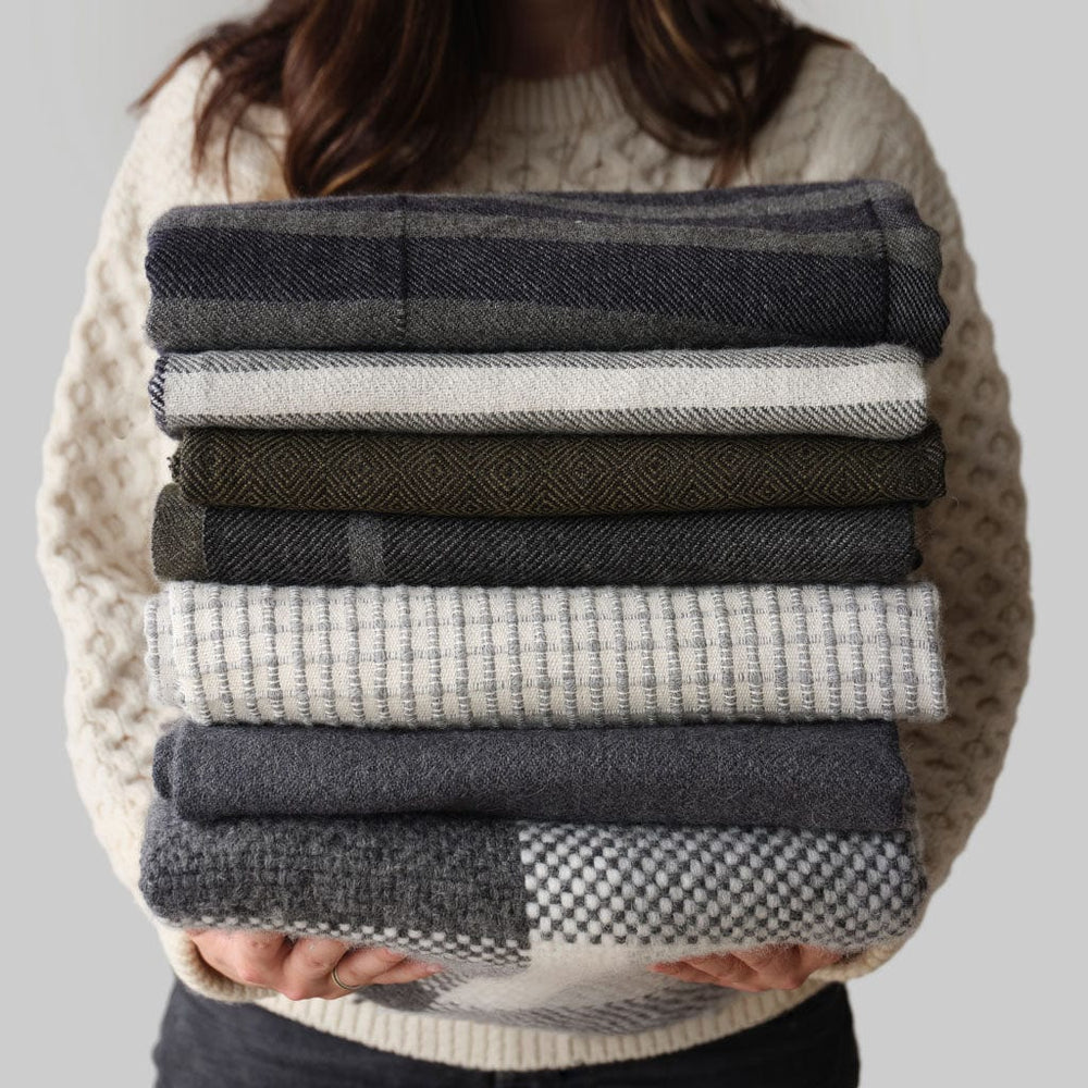 Stack of blue, grey, and cream throws held by model