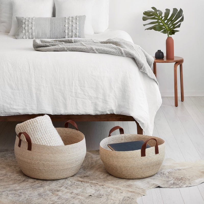 Medium and large woven palm floor baskets at the foot of a bed, natural