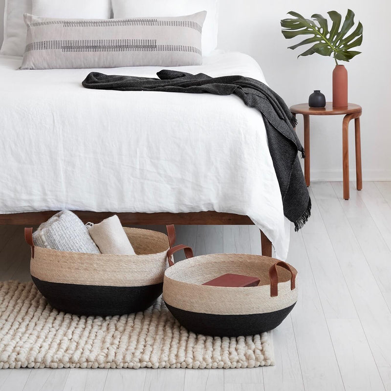 Color-blocked woven palm floor baskets at the foot of a bed, black