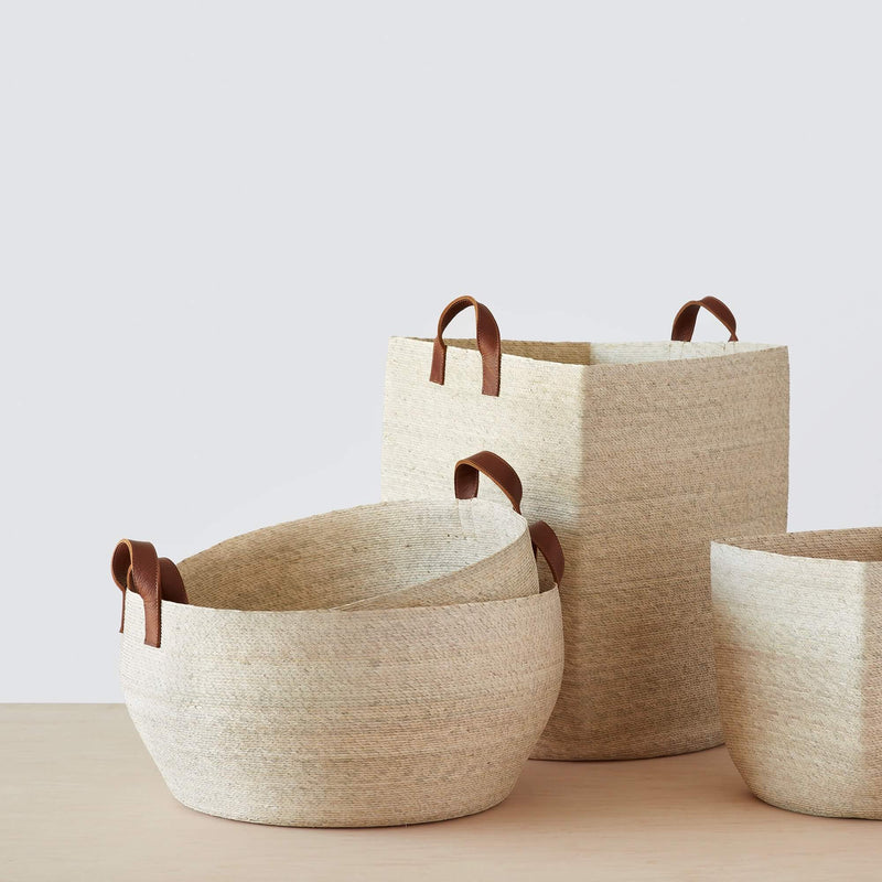 Group of light-colored woven storage baskets with leather handles, natural