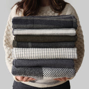 Stack of grey, cream, olive, blue alpaca throws held by model, navy