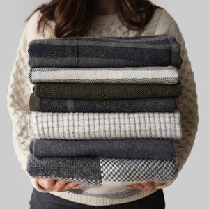 Stack of grey, cream, olive, blue alpaca throws held by model, navy