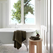 Green waffle towel draped over edge of bathtub, olive