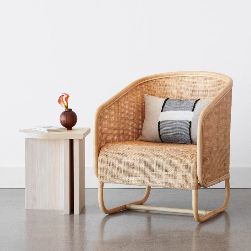 Woven pillow on cane chair next to wooden table, natural
