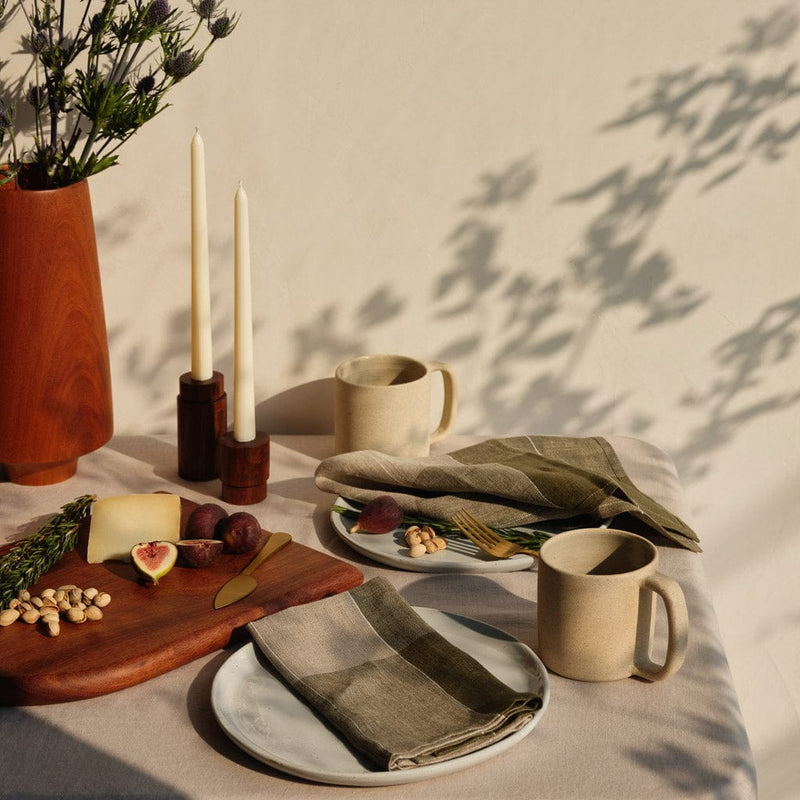 Styled tabletop with napkins and ceramic mugs, olive