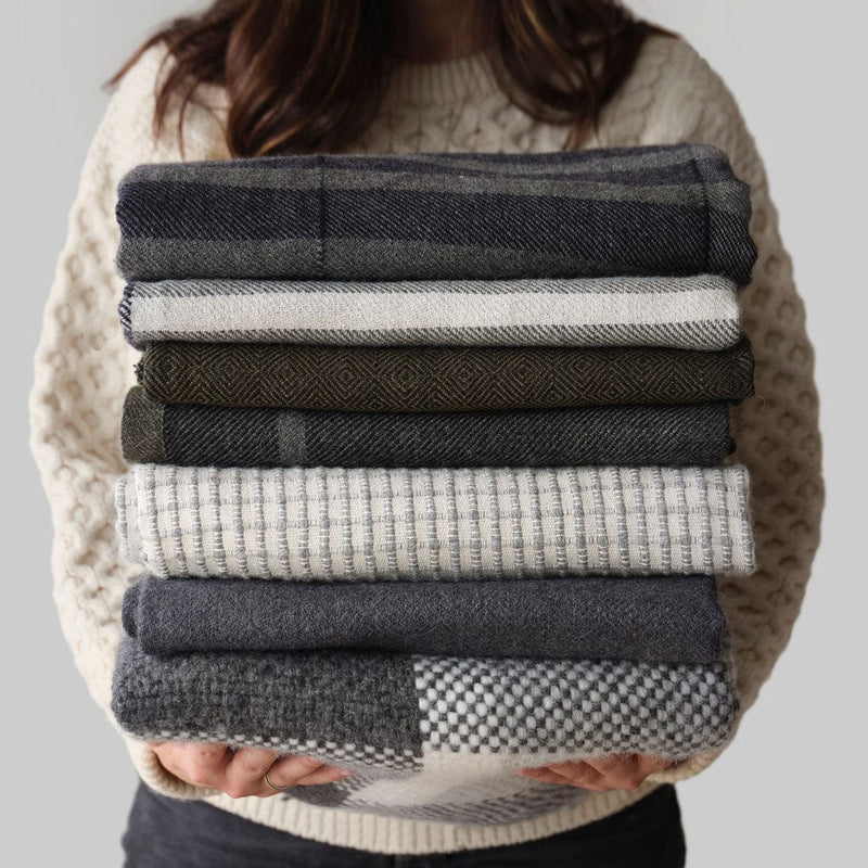 Stack of blue, grey, and cream throws held by model, olive-grey
