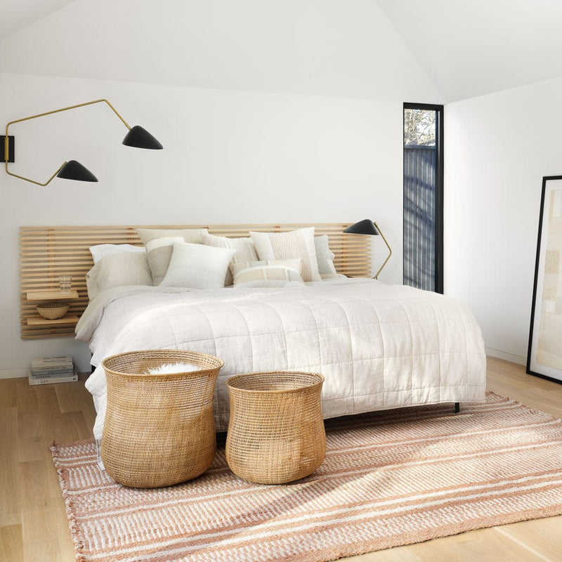 Woven baskets at foot of styled bed with sand thin striped linen quilt, sand-thin-stripe