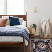 Styled bedroom with slate blue linen quilt folded at foot of bed, slate-blue