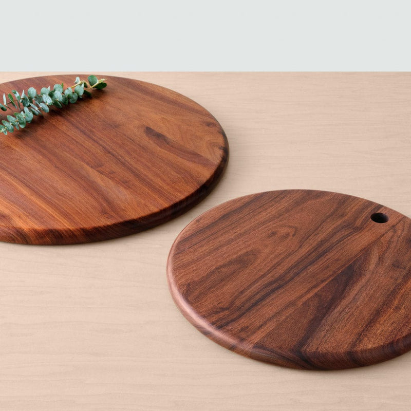 Two granadillo wood serving boards lying on counter with greenery, granadillo