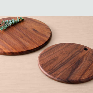 Two granadillo wood serving boards lying on counter with greenery, granadillo