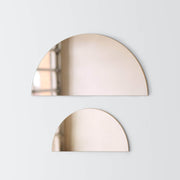 Large bronze half moon mirror hanging over small bronze half moon mirror