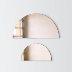 Large bronze half moon mirror hanging over small bronze half moon mirror